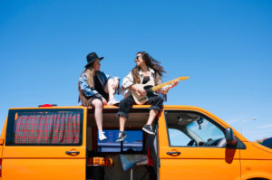 Two women sitting on roof of van, playing guitar Two women sitting on roof of van, playing guitar