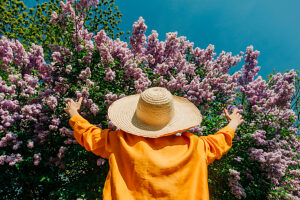Man in a straw hat and yellow shirt embracing a flowering purple lilac tree outdoors in a village setting