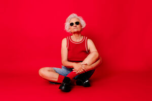 Senior woman in casual clothing and sunglasses sitting on a red background