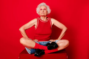 Senior woman in red outfit sitting cross-legged against a red background