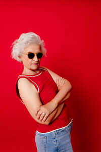 Woman in sunglasses and red top posing confidently against a red background