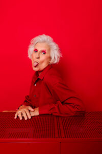 Playful woman in red shirt with white hair posing against a red background