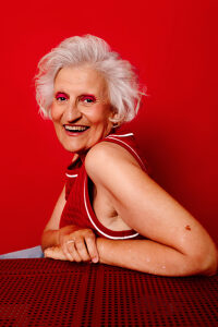 Smiling woman with white hair in red dress against red background