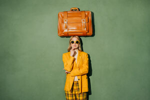 Stylish woman with suitcase on head in yellow outfit