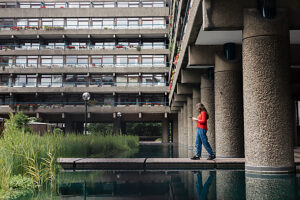 Woman using smartphone near brutalist building and pond