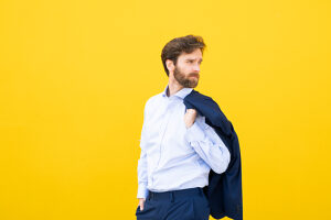 Confident businessman holding blazer against yellow background