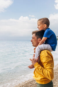 Father carrying son on shoulders enjoying a vacation by the sea