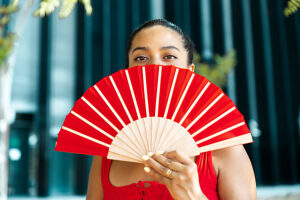 Stylish woman in red outfit posing with fan in elegant setting