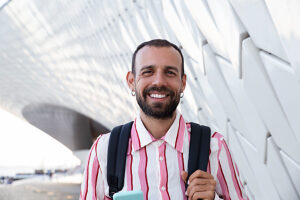 Smiling bearded person with backpack in front of modern architecture Lisbon