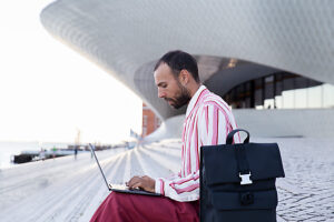 Professional working on laptop outdoors at Maat, Lisbon with backpack