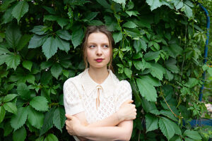 Portrait of happy woman in lace blouse outdoors surrounded by greenery