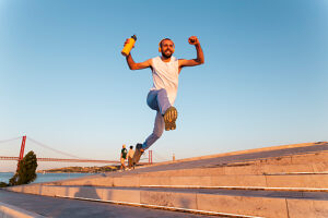 Happy man jumping outdoors with headphones and water bottle at sunset