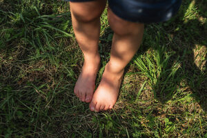 Barefoot child standing on grass in summer garden outdoors