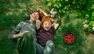 Mother and son with red hair laughing together on grass with berries
