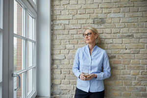 Businesswoman standing by window with drink in modern office