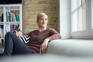 Businesswoman relaxing on sofa looking optimistic by window