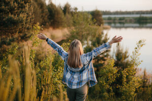 Woman enjoying hiking by a lake with arms raised in tranquil nature