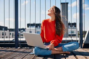 Woman sitting cross legged with laptop on sunny rooftop terrace