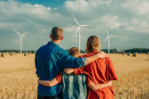 Family wearing jeans and cowboy hat hugging in wheat field near wind turbines