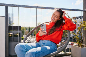 Smiling woman sitting on terrace using smartphone in sunny weather