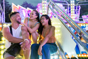 Friends sitting together laughing at an amusement park at night