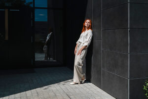 Red-haired woman leaning on urban wall outdoors in sunlight