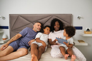 Interracial family playing with tablet together on bed in bedroom