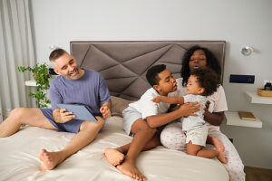 Interracial family in bedroom with children fighting over tablet