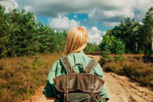 Rear view of woman with backpack walking on forest trail in Lower Silesia