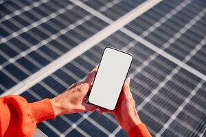 Close-up of hands holding smartphone with blank screen on solar panel rooftop