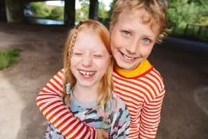 Siblings laughing and embracing outdoors in a carefree joyful moment