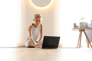 Frau 40+ praktiziert Yoga zuhause mit Notebook. Online Yoga Kurs. Frau 40+ praktiziert Yoga zuhause mit Notebook. Online Yoga Kurs.