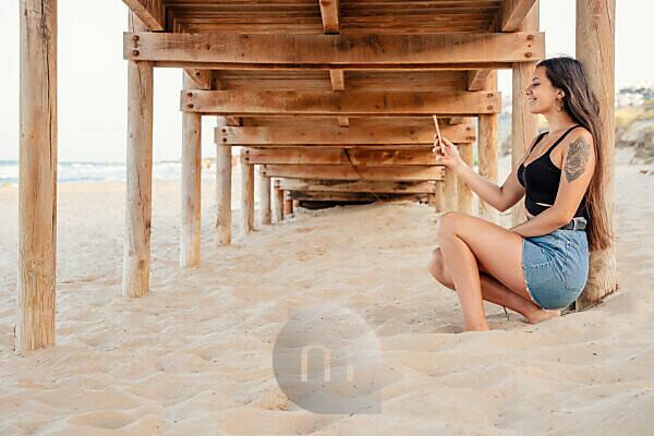 Teenage girl (16-17 years) wearing flip-flops sitting on tree