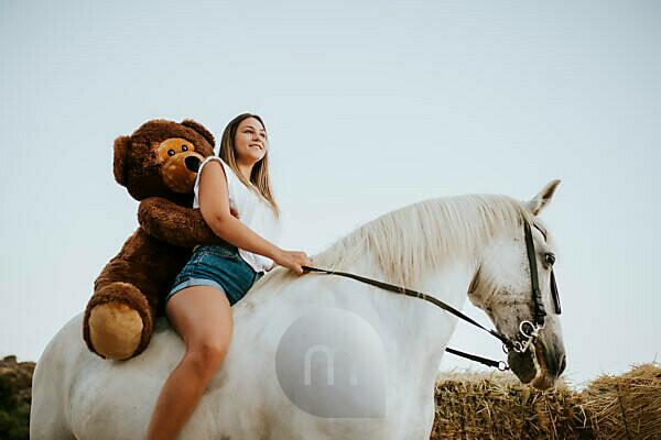 Portrait of beautiful young woman riding horse with large teddy