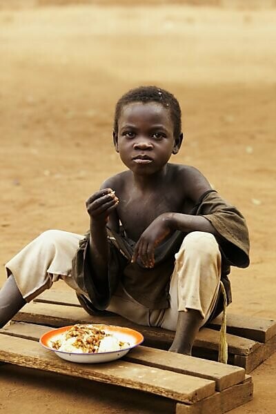 Bildagentur | mauritius images | A Boy Eats A Meal Sitting On