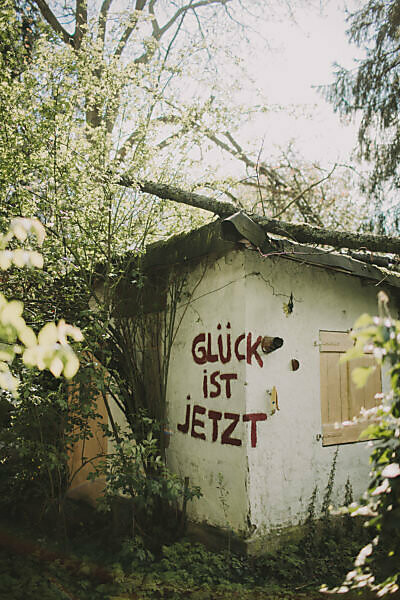 Old decayed garden house with the inscription 'Glück ist Jetzt' (Happiness is now) 