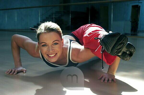 Brunette fat young girl in yellow hoodie and black leggings is trying to do  push ups while standing on her knees with crossed legs on violet mat  indoors. Concept of being in