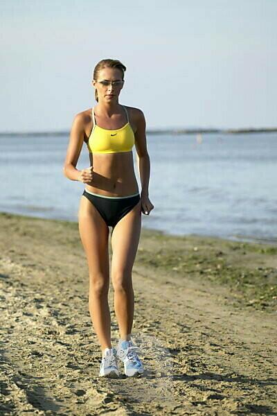 Strong, Fit, Sporty Woman, Wearing A Sports Bra And Fluorescent Shorts,  Standing On A Beach During A Short Break Of Her Training Run, With Her Hand  On Her Hip Stock Photo, Picture