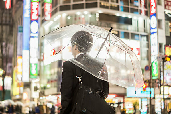 A businessman with an umbrella in the brightly lit streets in the evening