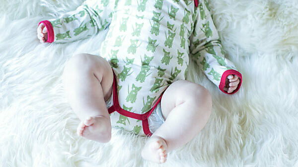 Baby, infant with bodysuit and bare legs lying on fur