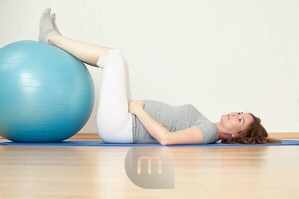 Peaceful young positive pregnant woman in gymnastic suit does yoga