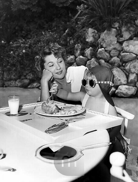 Bildagentur Mauritius Images Little Deborah Leslie Dozier Age 2 Devours Her Lunch While Her Mother Actress Joan Fontaine Eyes Fondly Her Daughter S Eating Outfit Of Sun Glasses And Jockey Cap