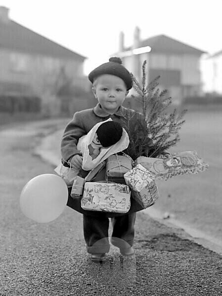 Small Child In Winter Clothing With Bobble Hat And His Arms Full Of Toys (Balloon With Toy Soldier And Christmas Tree-Also Lots Of Wrapped Gift Parcels)-He Is Walking Along The Pavement With Houses In The Background 5Th December 1934