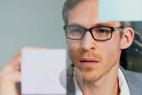 Young businessman reads Haftnotiz in windowpane, portrait