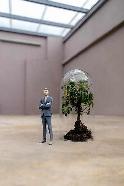 Businessman figurine standing by tree under a bell jar