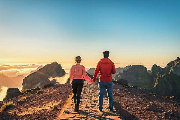 A couple walks hand in hand on Madeira over the mountain Pico do Arieiro. You can see the cloud cover at sunset.